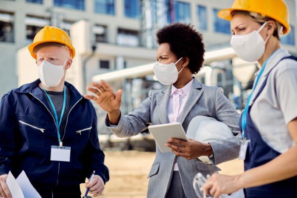 Ingeniería hidrológica; Arquitecta e ingeniera civil con mascarillas protectoras hablando en una obra de construcción.