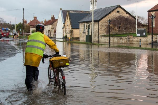 Riesgos hidrológicos; calle inundada y un señor pasando con su bicicleta.